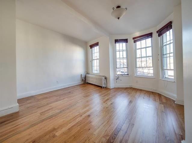 unfurnished room featuring radiator, wood finished floors, baseboards, and vaulted ceiling with beams