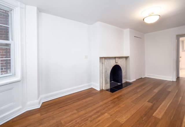 unfurnished living room with baseboards, a fireplace with flush hearth, and wood finished floors