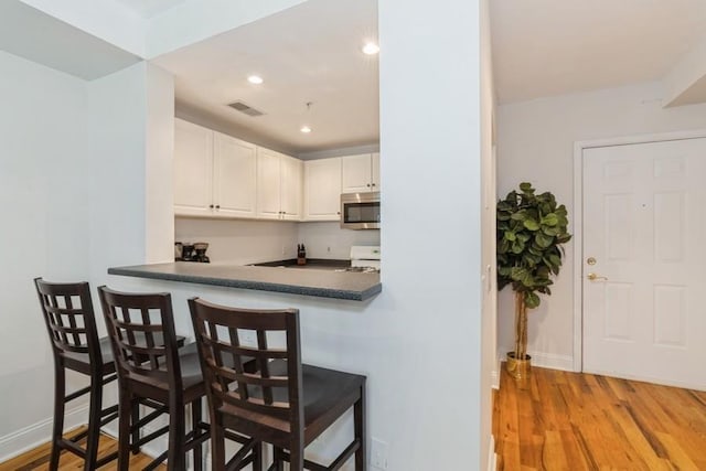 kitchen featuring stainless steel microwave, white cabinets, a breakfast bar, dark countertops, and visible vents