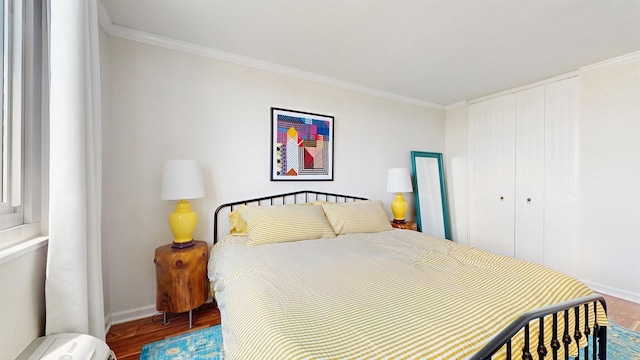 bedroom with a closet, baseboards, crown molding, and wood finished floors