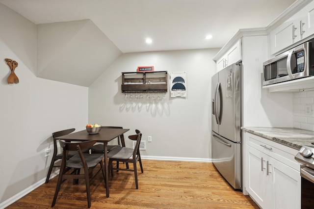 kitchen featuring white cabinets, light hardwood / wood-style flooring, decorative backsplash, light stone countertops, and appliances with stainless steel finishes