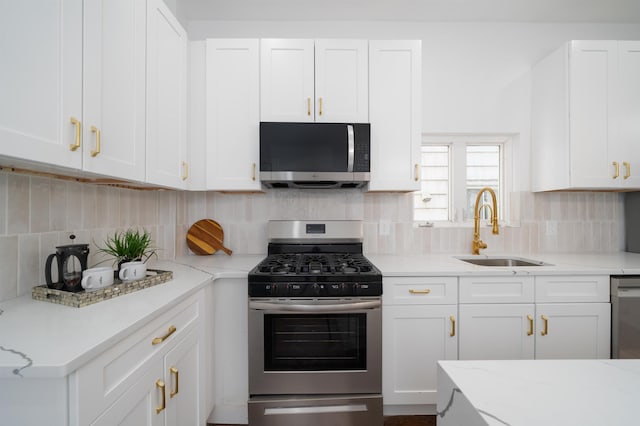 kitchen with light stone counters, appliances with stainless steel finishes, a sink, white cabinetry, and tasteful backsplash