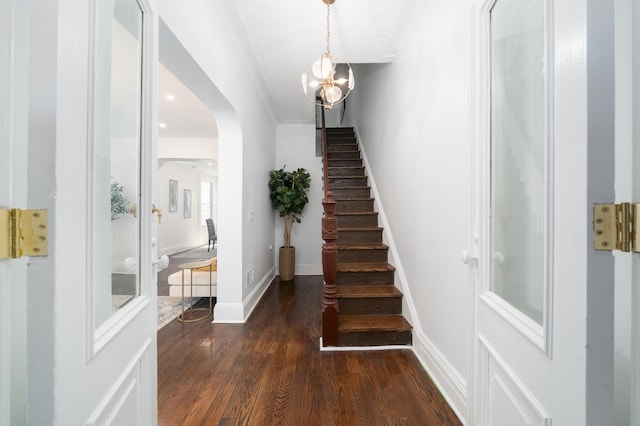stairs with crown molding, arched walkways, wood finished floors, baseboards, and a notable chandelier
