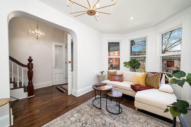 living room with arched walkways, wood finished floors, baseboards, a notable chandelier, and stairs