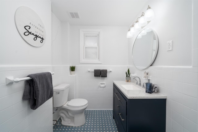 bathroom featuring visible vents, tile walls, wainscoting, vanity, and toilet