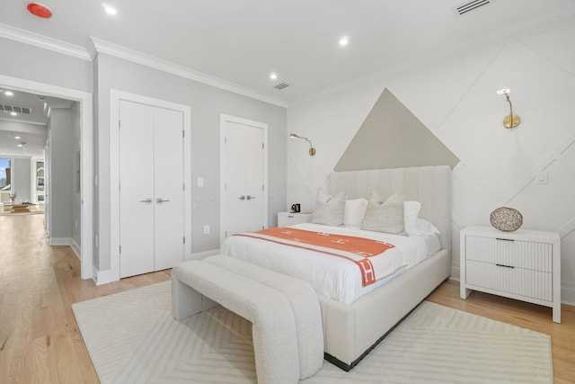 bedroom featuring light hardwood / wood-style flooring, crown molding, and multiple closets