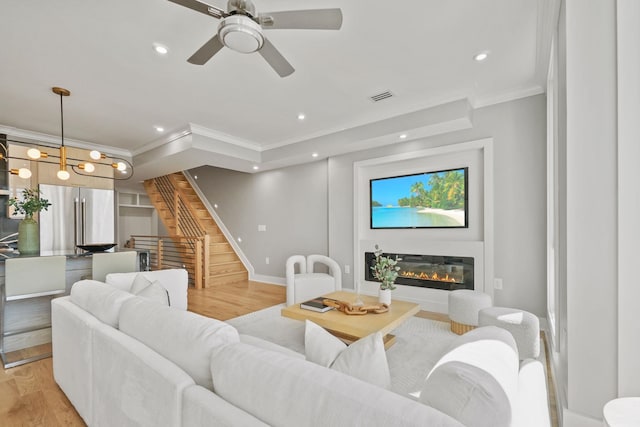 living room with crown molding, ceiling fan with notable chandelier, and light wood-type flooring