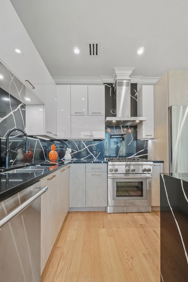 kitchen with decorative backsplash, light wood-type flooring, stainless steel appliances, and wall chimney exhaust hood