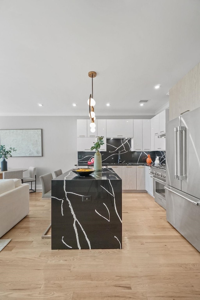 kitchen featuring pendant lighting, white cabinets, decorative backsplash, light wood-type flooring, and premium appliances