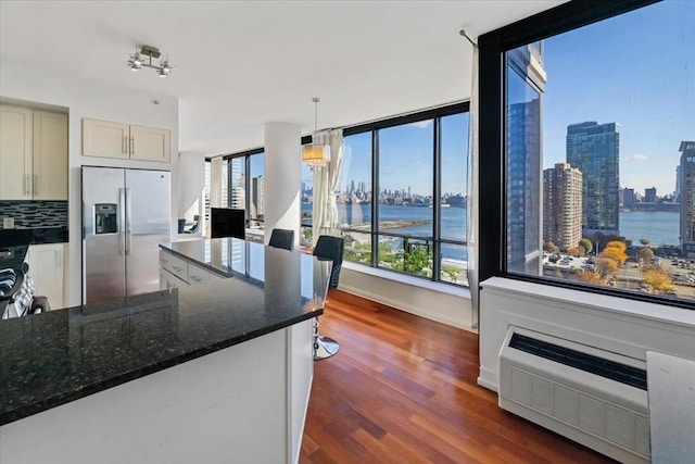 kitchen featuring dark wood-type flooring, a water view, dark stone countertops, decorative light fixtures, and stainless steel fridge with ice dispenser