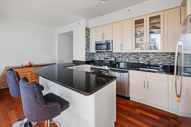 kitchen featuring kitchen peninsula, appliances with stainless steel finishes, dark hardwood / wood-style flooring, backsplash, and sink