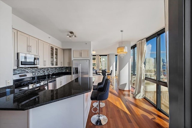 kitchen with hanging light fixtures, hardwood / wood-style flooring, appliances with stainless steel finishes, tasteful backsplash, and a notable chandelier