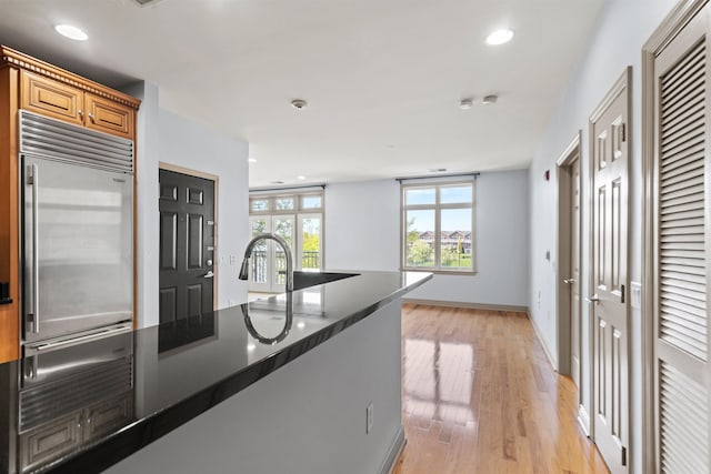 kitchen with brown cabinetry, stainless steel built in refrigerator, recessed lighting, baseboards, and light wood-style floors