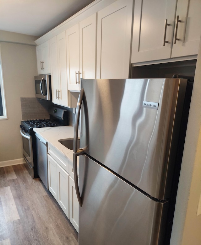 kitchen featuring light hardwood / wood-style floors, light stone counters, white cabinets, and stainless steel appliances