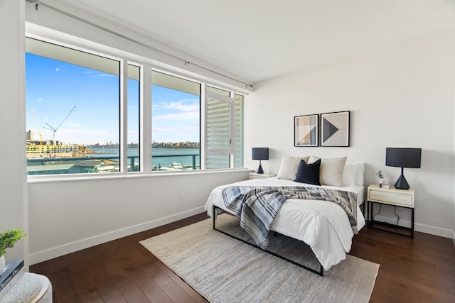 bedroom with a water view, wood finished floors, and baseboards