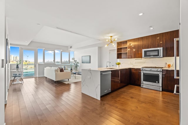 kitchen with appliances with stainless steel finishes, open floor plan, a sink, and wood finished floors