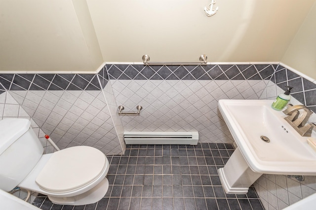 half bathroom with a sink, baseboard heating, tile walls, and toilet