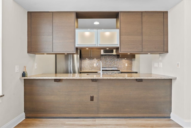 kitchen with sink, light hardwood / wood-style flooring, decorative backsplash, stainless steel refrigerator, and light stone countertops