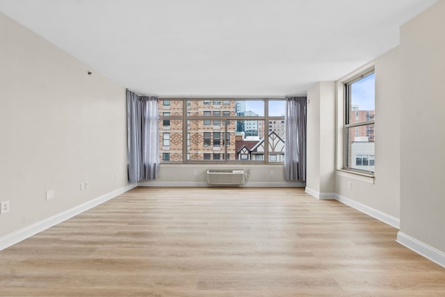 unfurnished room with a wall mounted AC, light hardwood / wood-style flooring, and a wealth of natural light