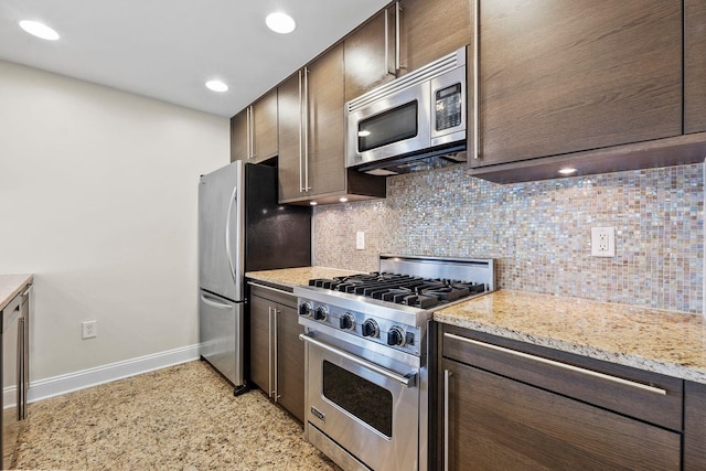 kitchen with stainless steel appliances, light stone countertops, dark brown cabinets, and decorative backsplash