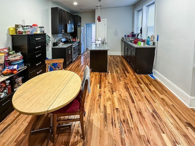 kitchen with light wood-type flooring, stainless steel appliances, a center island, sink, and light stone counters