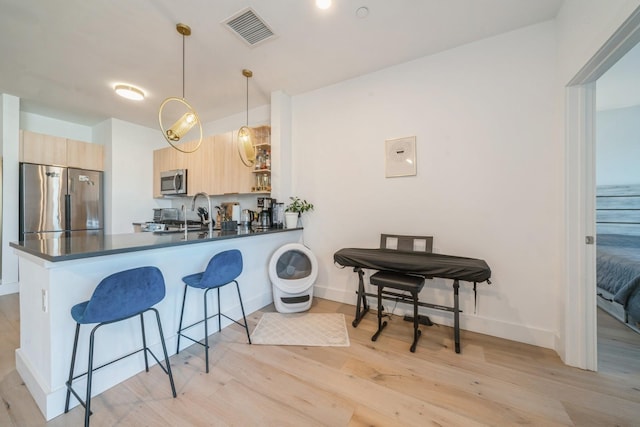 kitchen with visible vents, light brown cabinetry, dark countertops, stainless steel appliances, and a breakfast bar area