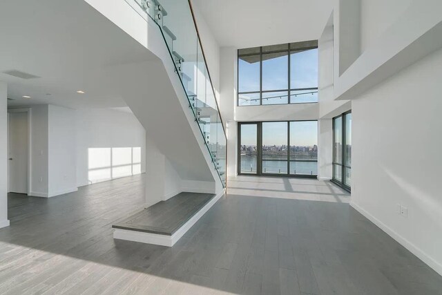 320 Adolphus Ave Unit 1415, Cliffside Park, NJ 07010 - unfurnished living room featuring a towering ceiling, baseboards, a water view, and wood finished floors