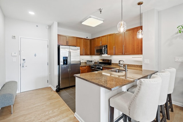 30 Freedom Way Unit 302, Jersey City, NJ 07305 - kitchen featuring stainless steel appliances, brown cabinetry, a peninsula, hanging light fixtures, and dark stone counters