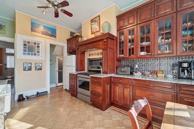 kitchen with stainless steel gas stove, backsplash, ornamental molding, white fridge, and light stone countertops