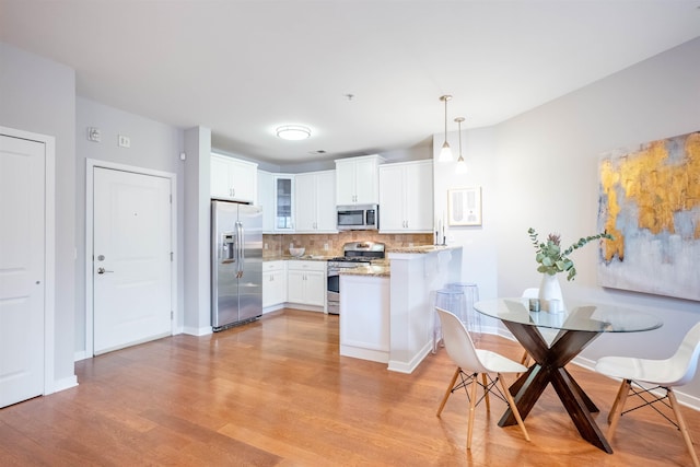 kitchen featuring stainless steel appliances, a peninsula, white cabinetry, light wood-type flooring, and glass insert cabinets