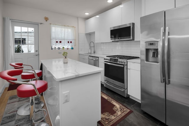 kitchen with sink, white cabinetry, a center island, appliances with stainless steel finishes, and backsplash