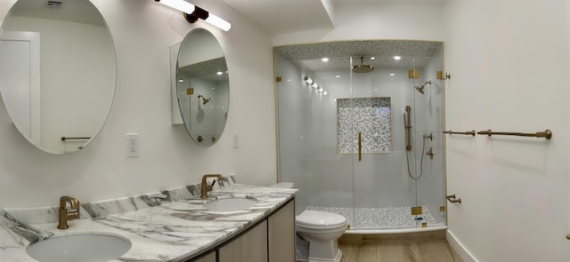 bathroom featuring a shower stall, double vanity, a sink, and toilet
