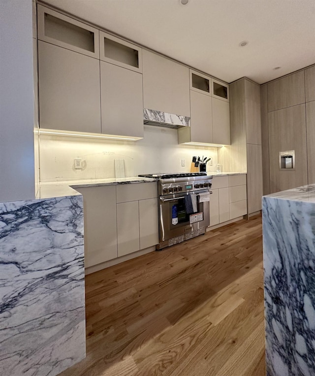 kitchen with high end stainless steel range oven, light wood-style flooring, modern cabinets, and glass insert cabinets
