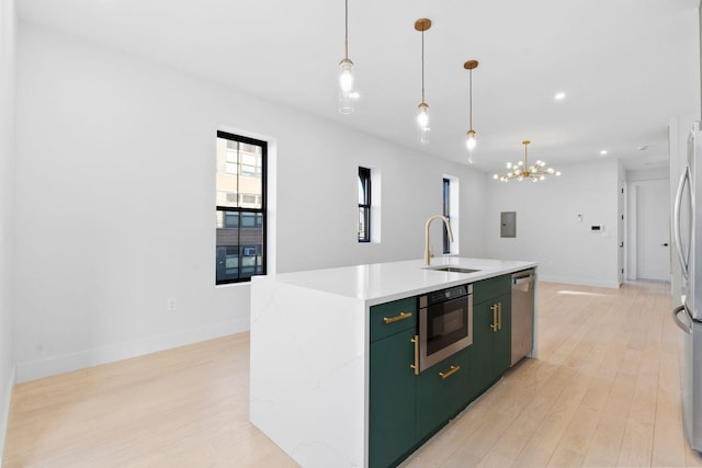 kitchen featuring decorative light fixtures, sink, stainless steel appliances, a center island with sink, and light wood-type flooring