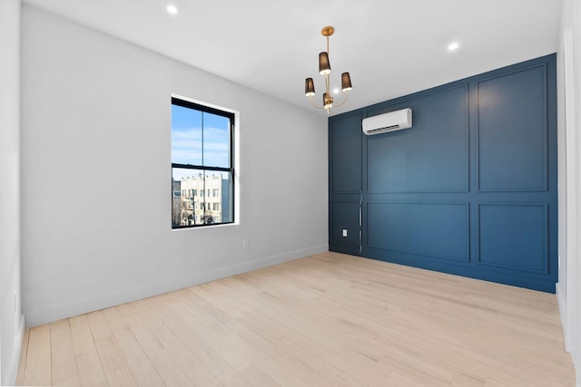 empty room featuring a wall mounted AC, a notable chandelier, and light hardwood / wood-style flooring