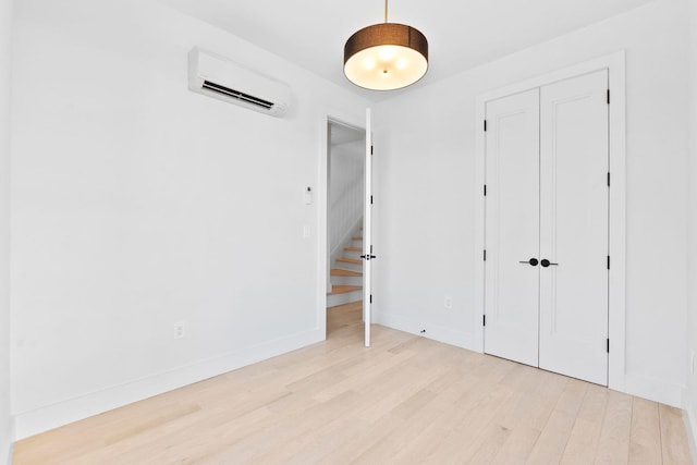 unfurnished bedroom featuring a closet, a wall unit AC, and light hardwood / wood-style flooring