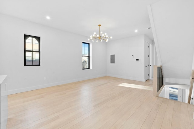 unfurnished living room featuring light wood-type flooring, electric panel, and an inviting chandelier