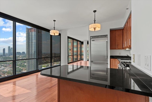 389 Washington St Unit 34E, Jersey City, NJ 07302 - kitchen with stainless steel built in fridge, dark countertops, brown cabinets, light wood-style floors, and decorative light fixtures