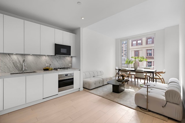 kitchen with light wood-style flooring, a sink, stainless steel appliances, light countertops, and decorative backsplash