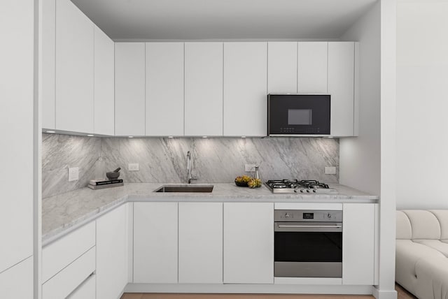 kitchen featuring backsplash, white cabinets, stainless steel appliances, and a sink