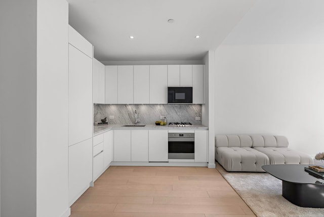 kitchen featuring light wood-style flooring, a sink, light countertops, appliances with stainless steel finishes, and tasteful backsplash