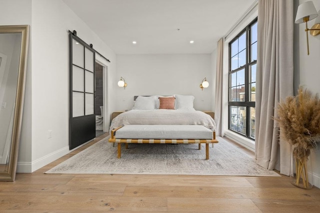 bedroom with multiple windows, a barn door, and light hardwood / wood-style flooring