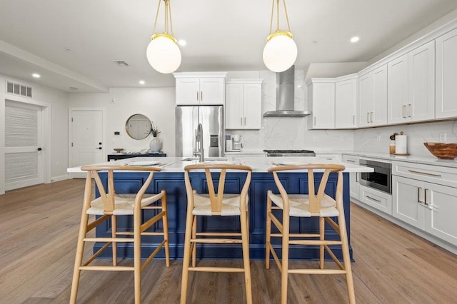 kitchen featuring wall chimney range hood, decorative light fixtures, and an island with sink