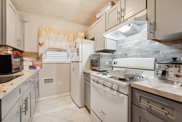 kitchen with gray cabinets, white appliances, light tile patterned floors, and tasteful backsplash