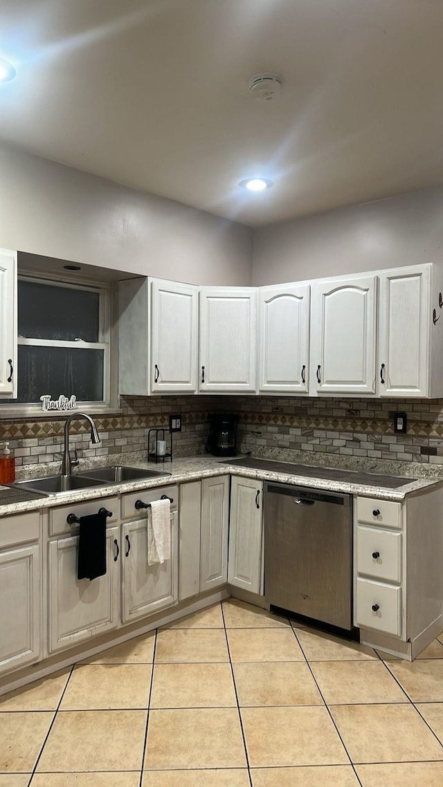 kitchen featuring decorative backsplash, stainless steel dishwasher, a sink, light tile patterned floors, and white cabinets