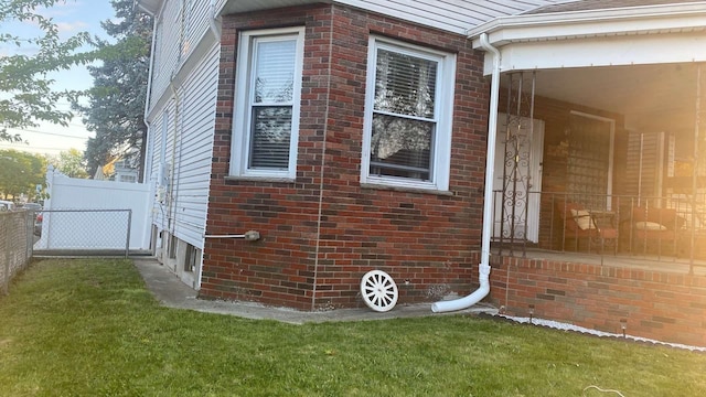 view of side of property featuring fence, a lawn, and brick siding