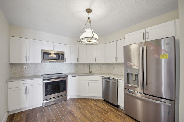 kitchen with stainless steel appliances, a sink, white cabinets, light stone countertops, and pendant lighting