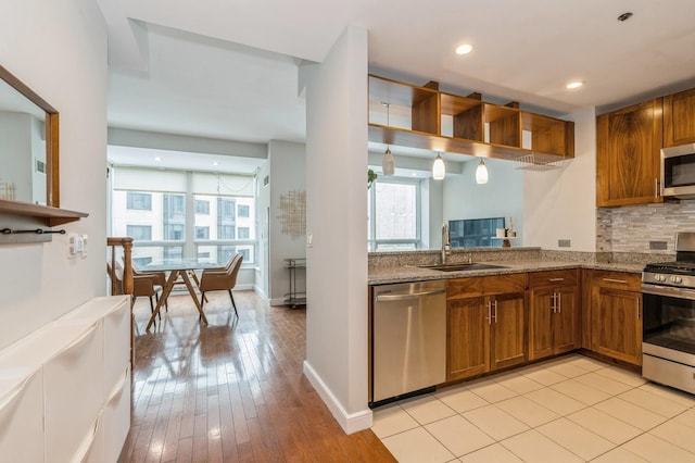 kitchen featuring sink, tasteful backsplash, appliances with stainless steel finishes, light stone countertops, and light hardwood / wood-style floors