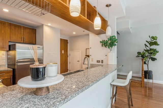 kitchen with a kitchen bar, light stone counters, hanging light fixtures, stainless steel refrigerator, and kitchen peninsula