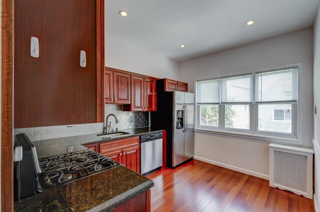 kitchen with sink, appliances with stainless steel finishes, dark brown cabinetry, decorative backsplash, and light wood-type flooring